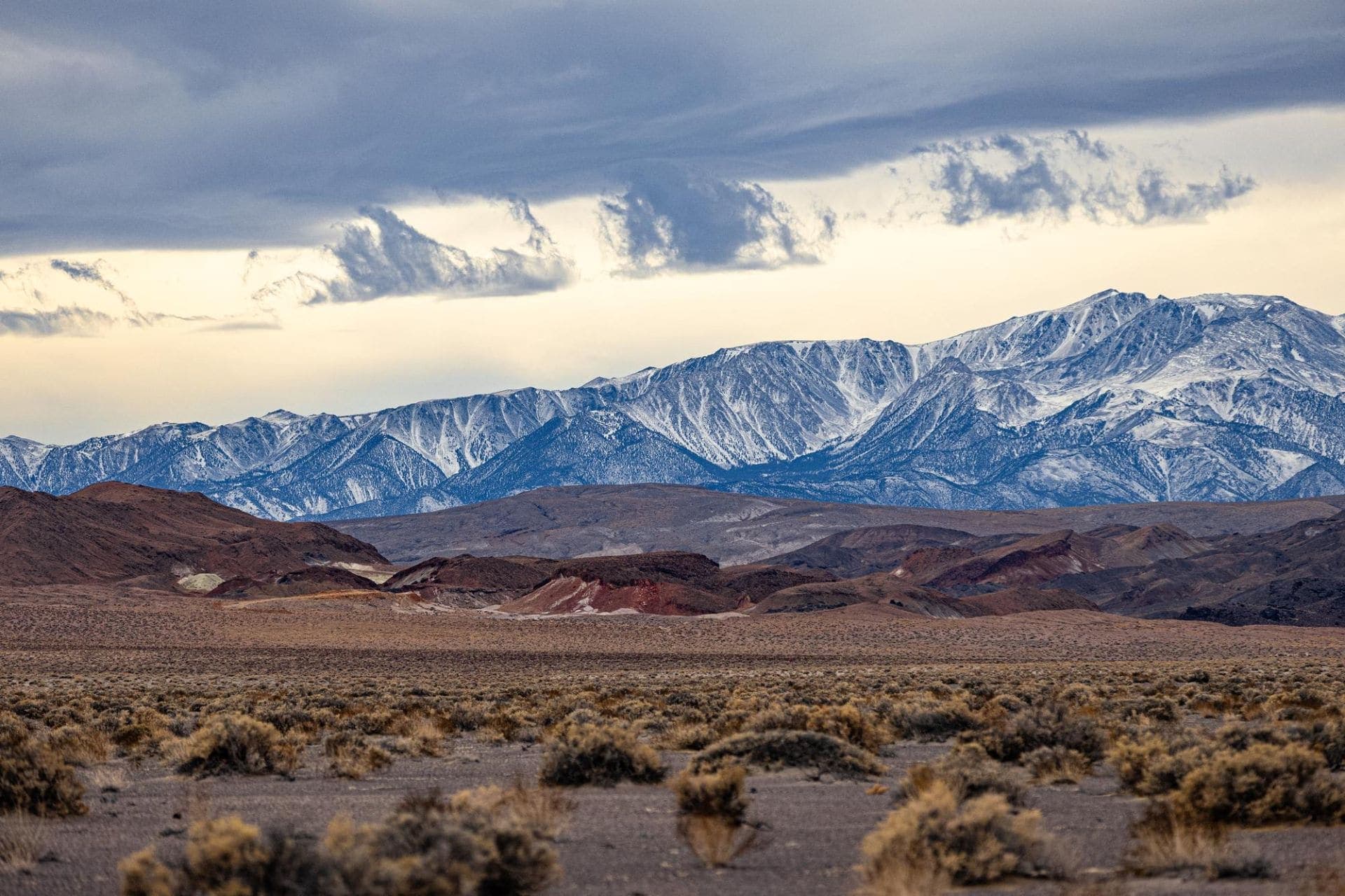 Snow-covered Sierra Nevada range under heavy clouds, seen across high desert sagebrush