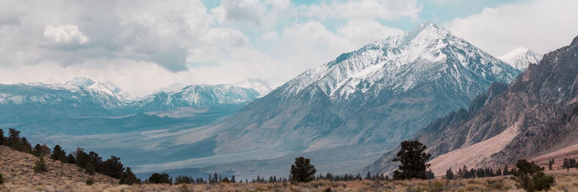 Wide view of snow-capped Sierra Nevada peaks above open high desert and scattered pines